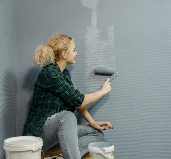 Woman using a roller to paint a wall grey during a home renovation project. Indoor setting.